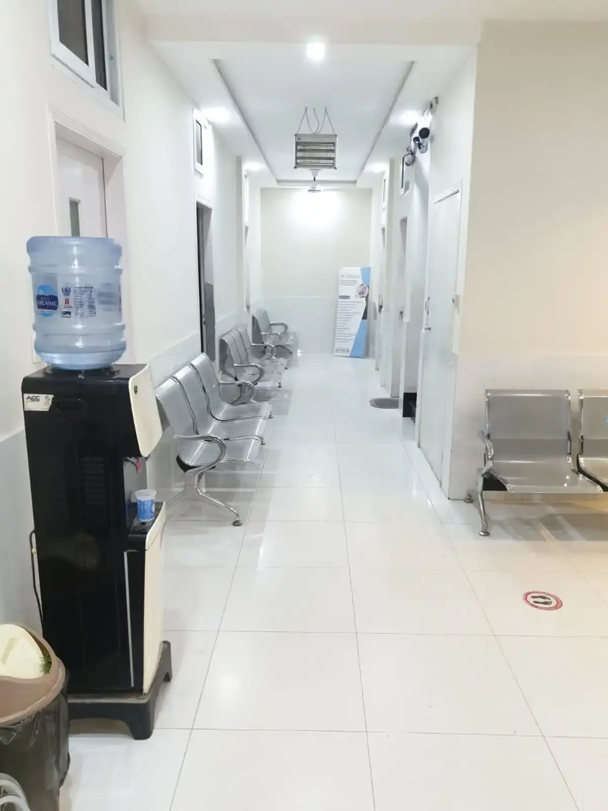 Clean, brightly lit corridor lined with metal waiting chairs and a water dispenser.