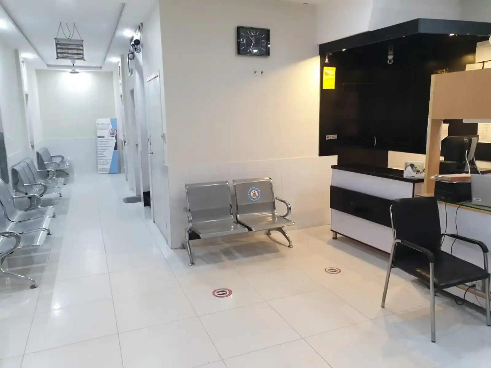 Reception and registration desk with a computer, waiting chairs, a wall clock and a tiled floor.